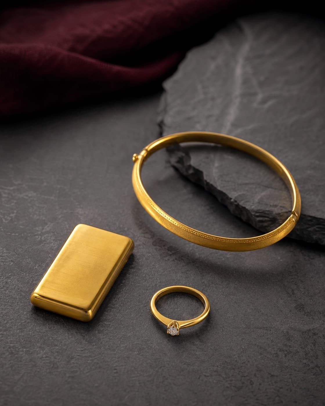 Gold bar, gelang dan cincin disusun di atas batu gelap